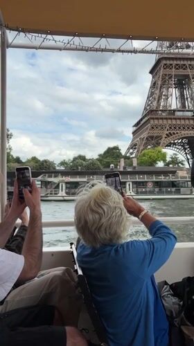 Tourists cruise Seine River, photograph Eiffel Tower on cloudy Monday