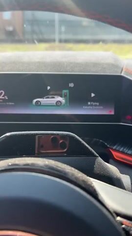 This video shows the interior of a car, focusing on the digital dashboard. The dashboard displays an orange electric car. The screen indicates that the car is charging and has 82% battery. It also shows the remaining range of 371 kilometers and an estimated charging time of 47 minutes. There are also options for camping mode, rest mode, and wash mode. The current temperature inside the car is 20.0 degrees Celsius. Outside, the sky is blue with some clouds, and a building or structure is visible in the background. The camera appears to be positioned behind the steering wheel, looking at the dashboard.
