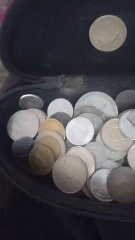 A video shows a close-up of coins in a container. The coins are gold and silver colored and appear to be in a pile. One coin in particular is shown in detail. It has a picture of a constellation on it and the word "AURIGA" written below it. The video is grainy and out of focus at times.