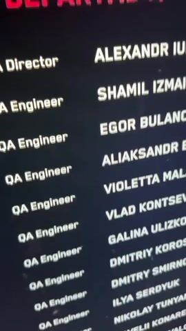 The video displays the credits of a film, video game, or similar project, shown on a screen in a dimly lit room. The text is white against a dark background. On the left side, the role "QA Engineer" is repeatedly listed. On the right side, corresponding names are visible, including: ALEXANDR IURCHIK (preceded by a partially visible "Director" role), SHAMIL IZMAILOV, EGOR BULANOV, ALIAKSANDR BARAVY, VIOLETTA MALASHENKO, VLAD KONTSEVYKH, GALINA ULIZKO, DMITRIY KOROSTYLEV, DMITRY SMIRNOV, ILYA SERDYUK, NIKOLAY TUNYAN, SAVELII KONAREV, and DARIA CHORNAYA (partially visible at the bottom). The screen itself shows some minor imperfections or dust. No people are visible. The setting appears to be an indoor environment, likely a home or screening room, given the dark surroundings. Music with a male vocalist is playing in the background. The scene is static, focusing on the scrolling credits.