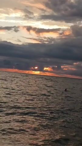 The video shows a body of water, possibly the ocean, with waves. The sky is cloudy with a sunset visible in the distance, casting an orange glow. There are no people or specific objects clearly identifiable in the video. The camera appears to be handheld and is moving slightly, suggesting it might be recording from a boat or a pier.