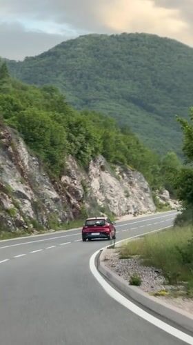 Red car travels mountain road near Vrela, Montenegro