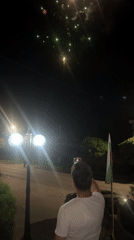 Person records fireworks display during nighttime street gathering