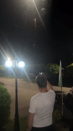 Person records fireworks display during nighttime street gathering