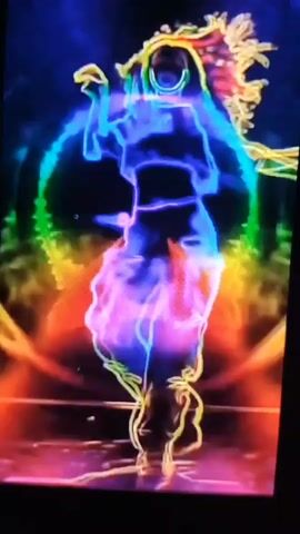 The video displays a neon-outlined figure dancing in front of a circular rainbow-colored light effect. The figure, depicted in a stylized, glowing outline, moves dynamically through various poses, including crouching, standing, and striking dramatic stances. The background is dark, with the luminous effects of the dancer and the rainbow circle being the primary visual elements. The lighting suggests a performance or gaming context.