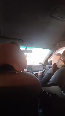 The video shows the inside of a moving car. A woman wearing a hijab is filming the interior of the car, including the driver and another female passenger. Loud music is playing. The person filming is holding the camera out to the side, towards the other passenger at times. The other passenger is also wearing a hijab. The driver is visible but not clearly seen.