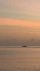 Traditional boats navigate calm Indonesian waters at colorful sunrise