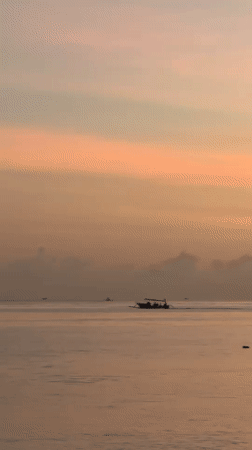 Traditional boats navigate calm Indonesian waters at colorful sunrise