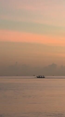 Traditional boats navigate calm Indonesian waters at colorful sunrise