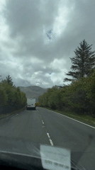 Driver records white van on tree-lined road toward hills