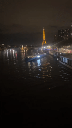 Boat cruises the Seine at night with the Eiffel Tower lit up