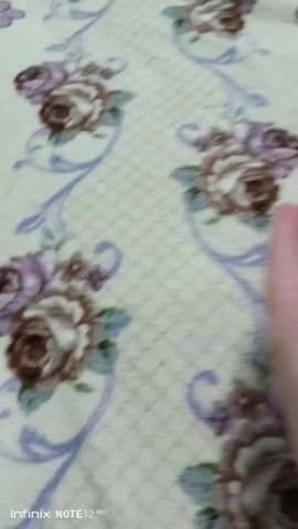 The video shows a close-up of a person's hand with a large, dark beetle on their wrist. The beetle appears to be a rhinoceros beetle. The person's hand is moving, and the beetle is seen crawling around on their wrist. The background is a light-colored fabric with a floral pattern. The video is taken from a first-person perspective.