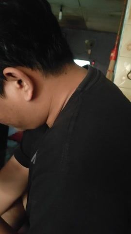 Here is a description of the video:

The video shows a person sitting on the floor in what appears to be a living room or similar space. The camera is pointed downwards, providing a close-up view of the person's head, shoulder, and hands.  They are wearing a black t-shirt and are focused on a smartphone in their hands. 

The camera pans down to reveal a green rug, a cup of coffee on a saucer, and an ashtray with a cigarette butt on the rug. There is also wooden furniture near the coffee, possibly a small table or stool. The environment is somewhat dimly lit.  The focus is mainly on the person using the smartphone and the items around them on the rug.