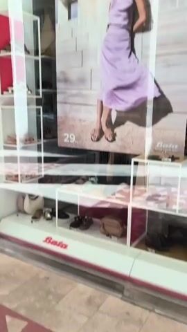 This is a video of a shoe store window display. The display features shoes, bags, and a large poster of a woman wearing a purple dress. The store's name, "Bata," is visible on the bottom of the window. There are also several shelves displaying different types of shoes. A sign in the window advertises "EXTRA -20%".
