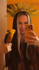 Woman with sunflower headband holds colorful parrot on thumb
