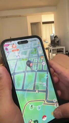 The video shows a close-up of a person holding a smartphone. The phone displays the interface of the game Pokémon GO. The initial frames show lists of Pokémon and raid battles. The phone screen then transitions to a map view of the game, followed by a detailed view of a Pokémon, identified as "Mega Mewtwo X" with a CP of 99273. The environment appears to be indoors, with furniture and lighting visible in the background.