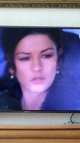 The media file shows a close-up of a young woman's face, captured from a television screen. The woman has dark hair and is wearing earrings. Her head is tilted, and she appears to be drinking from a straw in a clear cup, which is visible in the frame. The lighting is somewhat dim, casting a purplish hue over the scene. The background is dark and appears to be a solid color, possibly a blanket or wall. The woman's expression is neutral. There is a Samsung logo visible on the right side of the TV screen. The image is oriented vertically, suggesting it might have been taken with a phone camera or the TV screen is not positioned in a standard landscape orientation. The metadata indicates the location context is Turka, Ukraine. No specific time of day or weather conditions can be determined from the visual information.