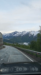 Driver travels wet mountain road with guardrails and concrete barriers