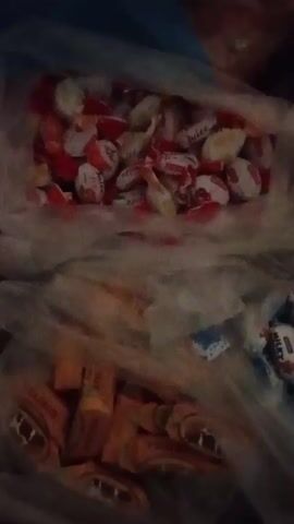 The video shows a close-up view into a semi-transparent plastic bag filled with different types of wrapped candy. The bag appears to be divided into sections. In the top section, there's a collection of round, red and white candies. In the bottom section, there's a collection of brown, rectangular candy bars. Moving right, there's a small collection of white and blue wrapped candies. The focus of the camera shifts between these sections.  The scene has a dark and somewhat indistinct quality.