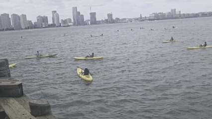 Kayakers paddle near NYC waterfront dock on overcast evening