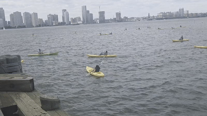 Kayakers paddle near NYC waterfront dock on overcast evening