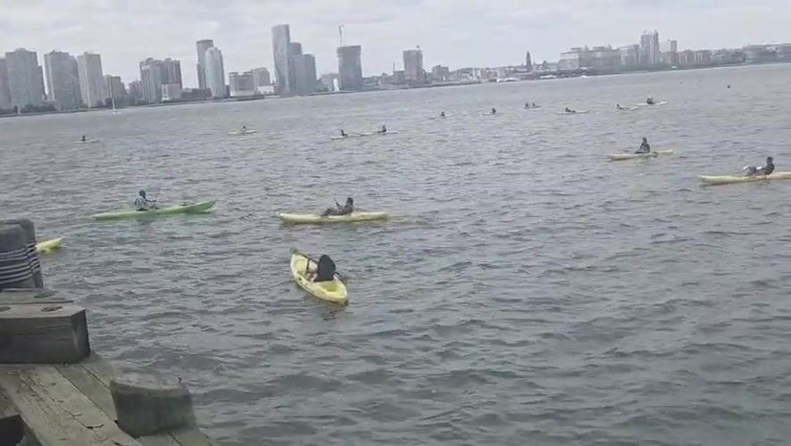 Kayakers paddle near NYC waterfront dock on overcast evening
