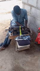 Man operates vintage sewing machine outdoors as child watches