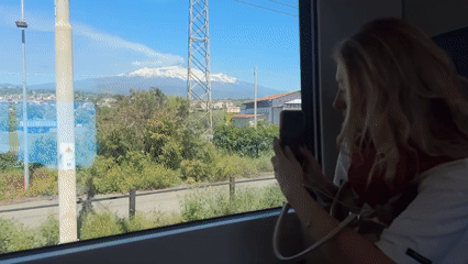 Train passenger photographs snow-capped Mount Etna near Acireale