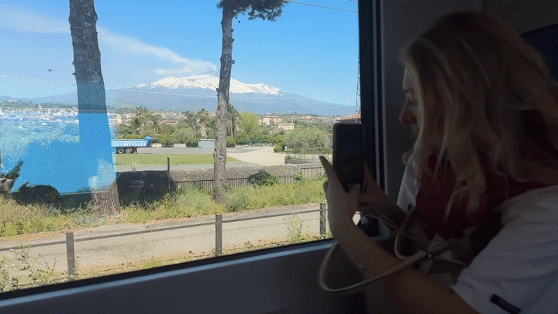 Train passenger photographs snow-capped Mount Etna near Acireale