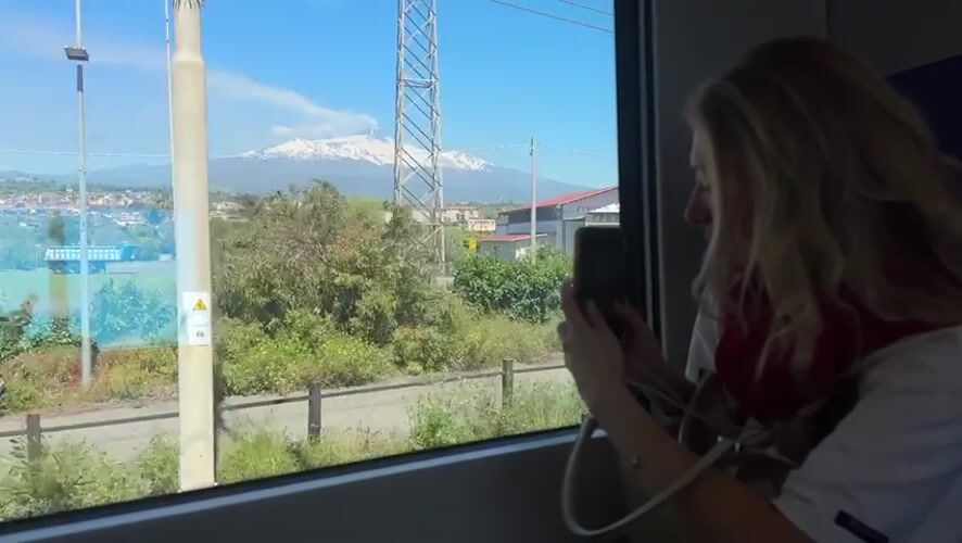 Train passenger photographs snow-capped Mount Etna near Acireale