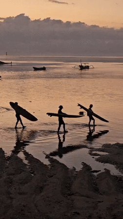 Dusk on a Denpasar beach — surfers, crowds, and calm water