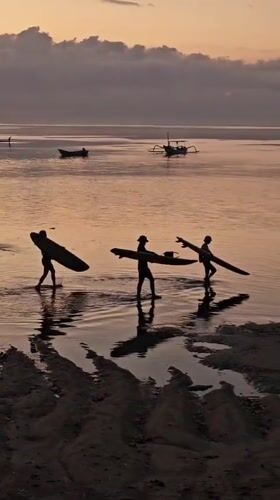 Dusk on a Denpasar beach — surfers, crowds, and calm water
