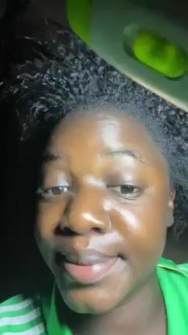 Here is a description of the video:

The video shows a person with dark skin and curly black hair under a bright light source. They are wearing a green shirt with white stripes. The person is smiling and looking at the camera, which appears to be very close to their face. They move the light around their face and hair. The background is dark and not easily discernible.