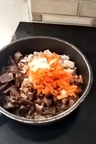 The video shows a cooking scene. The first shot is a close-up of a pot filled with chopped meat, carrots, and onions. The second shot is a close-up of a pan containing food being fried in oil. The food appears to be in bite-sized pieces and has a golden-brown color. The pan is on a stovetop, and the oil is bubbling around the food. A digital display on the stovetop shows the numbers 4 and 9. In the background, a mug with a floral pattern is visible.