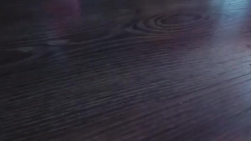 A sparkler is lit and held over a wooden surface. The sparkler flares and then begins to burn down. The sparkler is then moved and appears to be placed on the surface, before being moved again. The sparkler continues to burn, producing sparks, before the video cuts out.