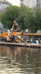 Construction crews work riverbank site with excavator, crane