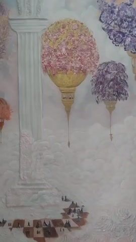 The video shows a close-up of a painting. The painting depicts a surreal, dreamlike scene with large, ornate floral arrangements hanging from what appear to be ornate lanterns. These lanterns are suspended in a cloudy, ethereal environment, with hints of classical architectural elements like a fluted column on the left. In the lower part of the painting, a group of tiny, silhouetted figures are walking across a checkered landscape, suggesting a sense of scale and perhaps a journey. The colors are soft and muted, with pinks, purples, golds, and whites dominating the palette.
