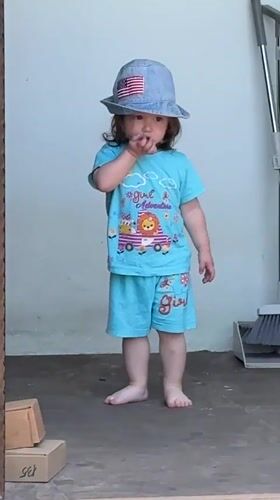Toddler plays barefoot in sunny Gudauta garden amid flowering plants