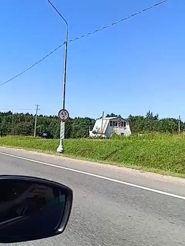 This video captures a view from a vehicle traveling on a road. The scene is dominated by a clear blue sky and a green, tree-lined landscape. A white car with a license plate is visible on the road. A sign with the number 4.5 in a red circle indicates a height restriction. There are power lines and poles scattered throughout the landscape. The video appears to be filmed on a sunny day.