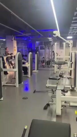 The video shows the interior of a gym with various workout machines. Some people are using the equipment. The gym has a blue lighting scheme. There are fire extinguishers visible in one of the shots.