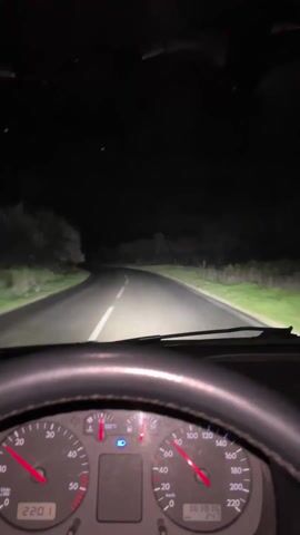 The video shows a person driving a car on a dark, empty road at night. The view is from the driver's perspective, focusing on the road ahead and the car's dashboard. The car's headlights illuminate the road, lined by trees on either side. The dashboard displays the car's speed, and engine temperature. The speedometer indicates the car is accelerating from 50 km/h to 100 km/h. Rap music is playing in the background.
