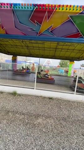 The video shows a bumper car ride at an amusement park. The bumper cars are small, electric vehicles with rubber bumpers that are designed to collide with each other. The ride is enclosed by a fence, and there is a canopy overhead to provide shade. The bumper cars are moving in a circular pattern, and people are seen riding in them. The overall scene is one of amusement and entertainment.