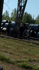 Workers operate crane to move metal rolls at warehouse
