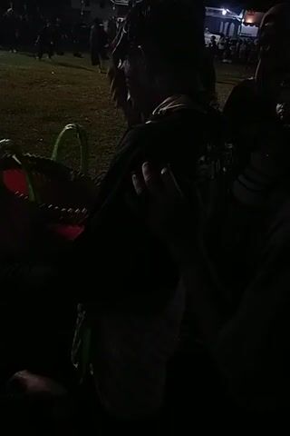 Here is a description of the video:

The scene is shrouded in darkness, with only faint illumination revealing some details. A group of people is gathered, though their faces are largely obscured. They appear to be near a green, curved object, possibly part of a playground or decorative structure. Someone is holding a red item with what looks like a green hoop attached. The overall atmosphere is unclear due to the lack of light, but the presence of people suggests a gathering or event.