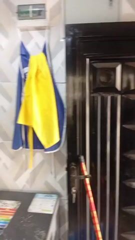 The video is a short pan around a kitchen. The first shot shows a stack of bowls on a counter, with a freezer underneath, and a blue and yellow apron hanging on the wall. The wall has a herringbone pattern. The next shot shows the counter, with various dishes and other objects stacked upon it. The next shot shows a four burner stovetop with two pots sitting on top of it, then the camera pans to show a countertop with canisters on it, next to the stove. The walls are the same herringbone pattern.