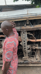 Two men work on overturned rusted vehicle in Nigeria