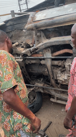 Two men work on overturned rusted vehicle in Nigeria