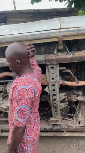 Two men work on overturned rusted vehicle in Nigeria