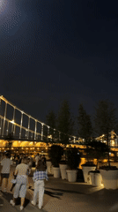 Nighttime riverfront stroll captured near illuminated suspension bridge