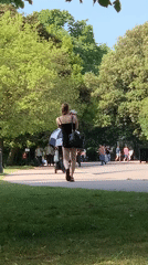 Woman walks through London park near harnessed white cat